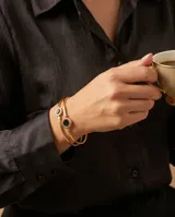 Esclava doble de acero con baño de oro, con dos círculos de esmalte negro y detalles de circonias. Cuenta con un sistema de apertura en la parte superior.