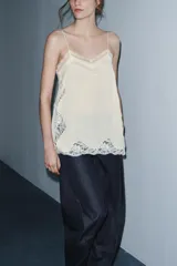 Top lencero de tirantes finos con escote en pico y aplicaciones de encaje a tono en el escote, laterales y bajo. Presenta aberturas laterales en el ruedo.