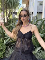 Top negro de encaje con breteles finos, detalle fruncido en el escote y abertura frontal cubierta por un nudo.