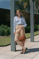 Cartera bandolera de cuero sintético color marrón con flecos largos en el frente y correa ajustable. Cierre superior con cremallera y herrajes metálicos color bronce.