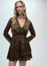 Vestido corto con cuello en V cruzado, mangas largas acampanadas y falda con volantes en el bajo. Presenta un estampado de textura tipo reptil en tonos marrones y negros, con cintura entallada.