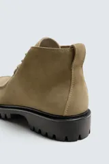 Bota de caña baja con cordones, confeccionada en piel con acabado de serraje. Presenta horma redonda, detalle de costura en el empeine y suela track con volumen.