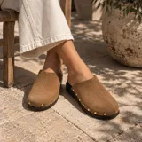 Zueco de gamuza color marrón con costura vertical en el empeine y tachas metálicas doradas alrededor de la suela.