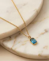 Collar de acero con baño de oro, compuesto por una cadena fina de eslabones y un dije rectangular con una circonia color celeste en el centro.