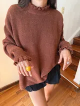 Buzo de punto oversize color rojo, con cuello alto y puños con terminaciones en volados. Presenta detalles en contraste color amarillo en el cuello y los puños, con un tejido de acabado ligeramente brillante.