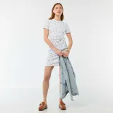 Vestido corto blanco con delicado estampado de pequeñas flores azules, de manga corta y cuello redondo. Presenta un diseño ajustado con un nudo decorativo fruncido en el lateral de la cintura.