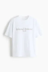 Remera oversized blanca de punto de algodón, con cuello redondo y hombros ligeramente caídos. Presenta un estampado frontal con la inscripción "island breeze IBIZA, 1998".