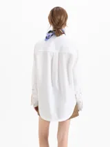Camisa de poplin color crema, de corte clásico con cuello camisero, mangas largas y cierre frontal con botones dorados de media esfera.