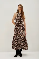 Vestido largo con estampado de leopardo en tonos negro y beige. Presenta cuello alto con detalle de frunce, tirantes anchos y cintura fruncida con elástico. La falda es larga con un volante en el ruedo.