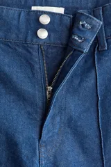 Jean de tiro alto con pierna amplia y corte tobillero. Confeccionado en denim de algodón con leve elasticidad, presenta un pliegue cosido vertical en el frente, cierre con botón y bolsillos traseros de parche.