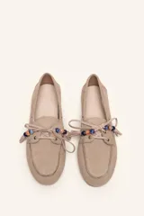 Mocasín estilo náutico de gamuza marrón, con cordones de cuero, borla decorativa y cuentas de colores en el empeine.