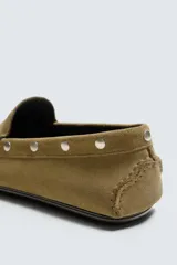 Mocasín de vestir para hombre confeccionado en piel con acabado de serraje en color mostaza. Presenta un diseño de horma redonda con detalle de tachas metálicas en los laterales y suela de goma flexible.