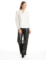 Blusa de seda fría color negro, con escote en V y lazo decorativo al cuello. Presenta mangas largas abullonadas con puños elásticos y detalles de strass aplicados en cuello, lazo y mangas.