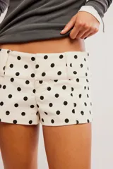 Short corto de algodón color beige claro con estampado de lunares negros, tiro bajo, cintura ancha con pasadores para cinturón, cierre de cremallera con gancho y costuras de estilo sastrero.