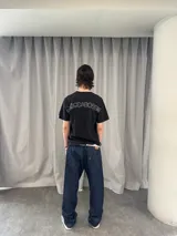 Remera de algodón color negro con estampado serigráfico en tono gris oscuro en la parte posterior. Presenta cuello reforzado, costuras reforzadas y una pequeña etiqueta decorativa en la manga.