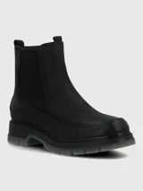Bota corta tipo Chelsea de cuero negro, con elásticos laterales y suela track gruesa de goma translúcida gris.