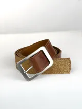 Cinturón de cuero genuino en tono tostado con acabado texturizado y detalles dorados. Presenta una hebilla circular metálica en color dorado mate.