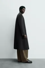 Levita negra de corte relajado confeccionada en tejido con lana. Presenta cuello sin solapa, mangas largas con puños abotonados, bolsillo de vivo en el pecho y bolsillos con solapa en la cadera. Incluye bolsillos interiores, abertura en el centro de la espalda y cierre frontal con botonadura.