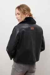 Chaqueta corta color beige con cuello de piel sintética negra, cierre frontal de botones y bolsillos laterales.