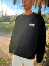 Buzo negro de algodón con interior confortable y calce relajado. En la espalda presenta un diseño en blanco con la inscripción "Dropz Corp." en tipografía script, la silueta de un ángel en trazo fino, texto pequeño y un código de barras. En el frente, lleva un logo sutil de Dropz al pecho.