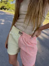 Shorts de tela a rayas verticales, con diseño patchwork en colores amarillo, naranja y celeste. Presenta cintura elástica y logo bordado en la pierna izquierda.