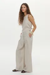 Pantalón de lino color beige, de pierna amplia, con elástico en la cintura, pinzas en el frente y bolsillos laterales y traseros.