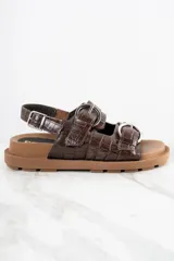 Sandalias bajas color marrón con textura croco, dos tiras anchas sobre el empeine con hebillas metálicas plateadas y tira trasera ajustable con hebilla.