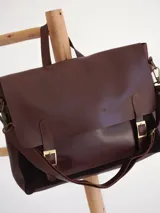 Maletín tipo cartero con solapa de cuero marrón y cuerpo de gamuza azul. Cuenta con correas ajustables con hebillas metálicas, asa superior y correa larga para llevar al hombro.