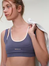 Top deportivo rosa con efecto layering, escote redondo bajo y tirantes dobles. Presenta el logo de la marca en tono oscuro en el frente.