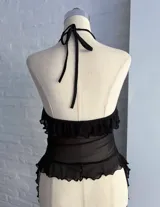 Top halter negro de microtul transparente, con escote en V profundo y bordes con volados o festones. Presenta un cierre frontal central.