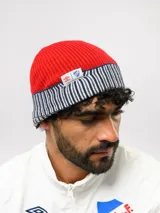 Gorro tipo beanie de punto acanalado en color azul marino, con vuelta en color rojo y blanco a rayas. Incluye etiqueta lateral con el logo de Umbro y el escudo del Club Nacional de Football.