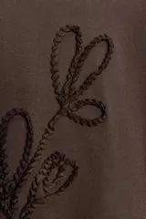 Camiseta de algodón color marrón oscuro, de corte regular, cuello redondo y manga corta. Presenta un detalle de lazos con tejido en relieve en el frente.