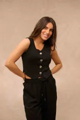 Top negro de tejido acanalado, sin mangas, con escote en V y cierre frontal de cuatro botones metálicos plateados con relieve. Su diseño presenta un dobladillo inferior en punta.