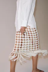 Falda midi de punto crochet en color crudo, con diseño de red, cintura elástica y bajo terminado en flecos largos.
