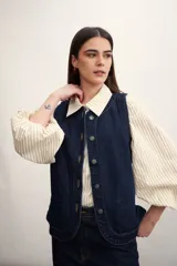 Chaleco azul de denim con cuello en V y cierre frontal con botones metálicos. Posee bolsillos delanteros y corte clásico.
