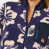Campera de polar con cierre frontal, diseño estampado de flores tipo hibisco en tonos azul y crema. Cuenta con cuello alto, bolsillo frontal con cierre en el pecho y bolsillos laterales, con detalle de logo de la marca en el bolsillo superior.