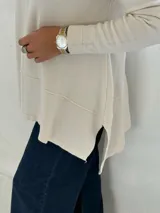 Sweater de punto color beige con cuello alto tipo polera, diseño holgado y costuras visibles en el frente.