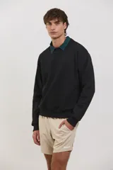 Buzo de algodón rústico color negro con cuello redondo y detalle de cuello tipo polo en color verde oscuro debajo. Presenta puños y ruedo acanalados, con un diseño de calce clásico.
