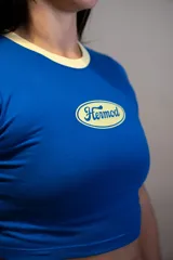 Remera corta de manga corta, color azul vibrante, con cuello redondo y ribetes en color crema. Presenta un logo ovalado centrado con el texto "Hermod" en tipografía cursiva.