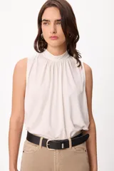 Blusa sin mangas color crema, con cuello alto fruncido y diseño holgado.