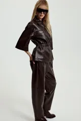 Pantalón de tiro alto confeccionado en material efecto piel, con cintura elástica ajustable mediante cordones, bolsillos delanteros y bolsillos de plastrón en la parte trasera.