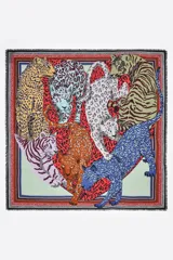 Chal cuadrado confeccionado en modal con un diseño estampado de diversos felinos, como tigres y leopardos, dispuestos en forma de corazón sobre un fondo rojo. Presenta bordes decorativos con marcos en contraste y terminaciones desflecadas.