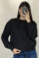 Buzo de cuello redondo y manga larga, color negro, con diseño de pequeños puntos brillantes distribuidos por toda la prenda. Presenta puños y ruedo acanalados.