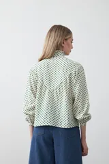 Camisa de viscosa con estampado de lunares, cuello alto con volados y cierre frontal de botones. Presenta un diseño de silueta suelta con frunces que aportan volumen y mangas largas con puños ajustados.