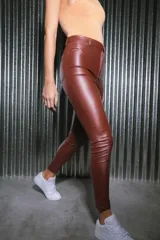 Pantalón de tiro alto confeccionado en bengalina engomada con acabado brillante. Presenta un diseño ajustado tipo chupín con cierre frontal, botones y remaches metálicos.