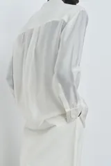 Camisa de mujer fluida de ZARA WOMAN COLLECTION, confeccionada en hilatura con mezcla de lyocell. Presenta escote en pico, manga larga con puños marcados y bajo asimétrico, con cierre frontal de botones ocultos.