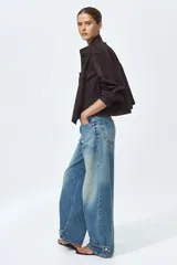 Jean de cinco bolsillos en denim de algodón rígido, con piernas maxivolumen de diseño curvo y corte estándar de cadera a muslo, ligeramente ceñidas en el bajo mediante trabilla. Cuenta con cintura de tiro alto, cierre y botón.