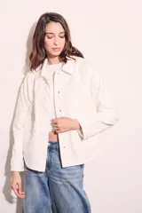 Sobrecamisa color blanco hueso de algodón, con cuello camisero, cierre frontal con botones a presión metálicos, bolsillos de parche en el pecho y bordados florales en los hombros. Corte holgado.