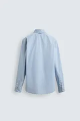 Camisa de hombre de manga larga, corte relajado (relaxed fit), color celeste con patrón de cuadros pequeños en azul y rojo. Presenta cuello abotonado (button-down), bolsillo de parche en el pecho y cierre frontal de botones.
