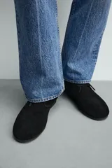 Bota tipo derby de caña baja, confeccionada en piel con acabado de serraje en color negro. Presenta cierre de cordones, horma redonda y suela de goma Vibram.